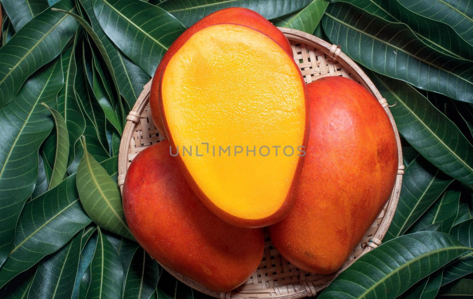Fresh Mango - Juicy diced fruit in bamboo sieve on green color leaves background. Tropical summer concept. Top view, close up, macro, copy space.