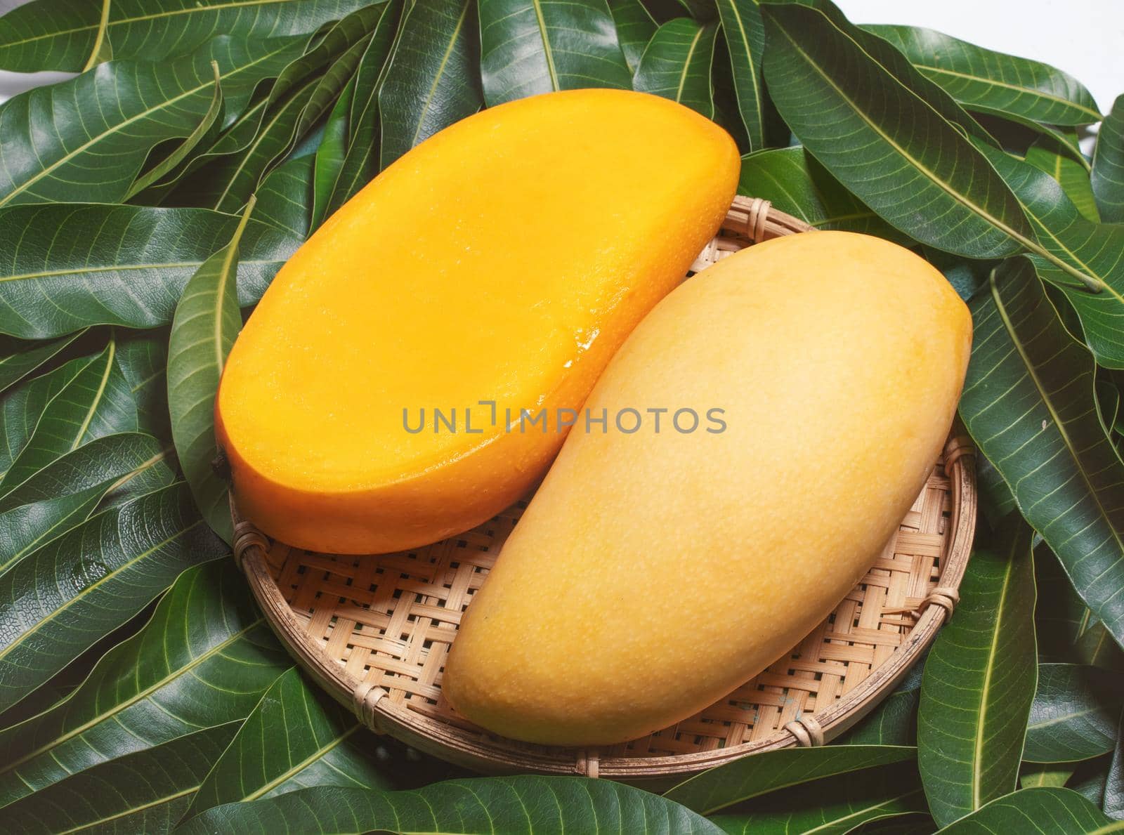 Fresh Mango - Juicy diced fruit in bamboo sieve on green color leaves background. Tropical summer concept. Top view, close up, macro, copy space.