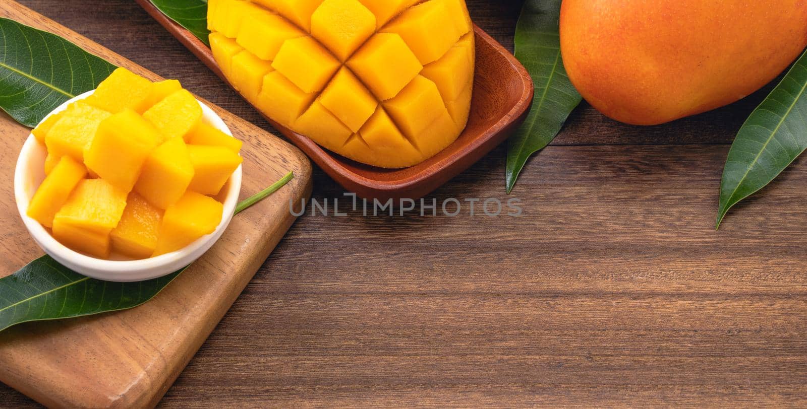 Fresh chopped mango cubes on wooden cutting board and rustic timber background. Tropical summer fruit concept, close up, macro, copy space.