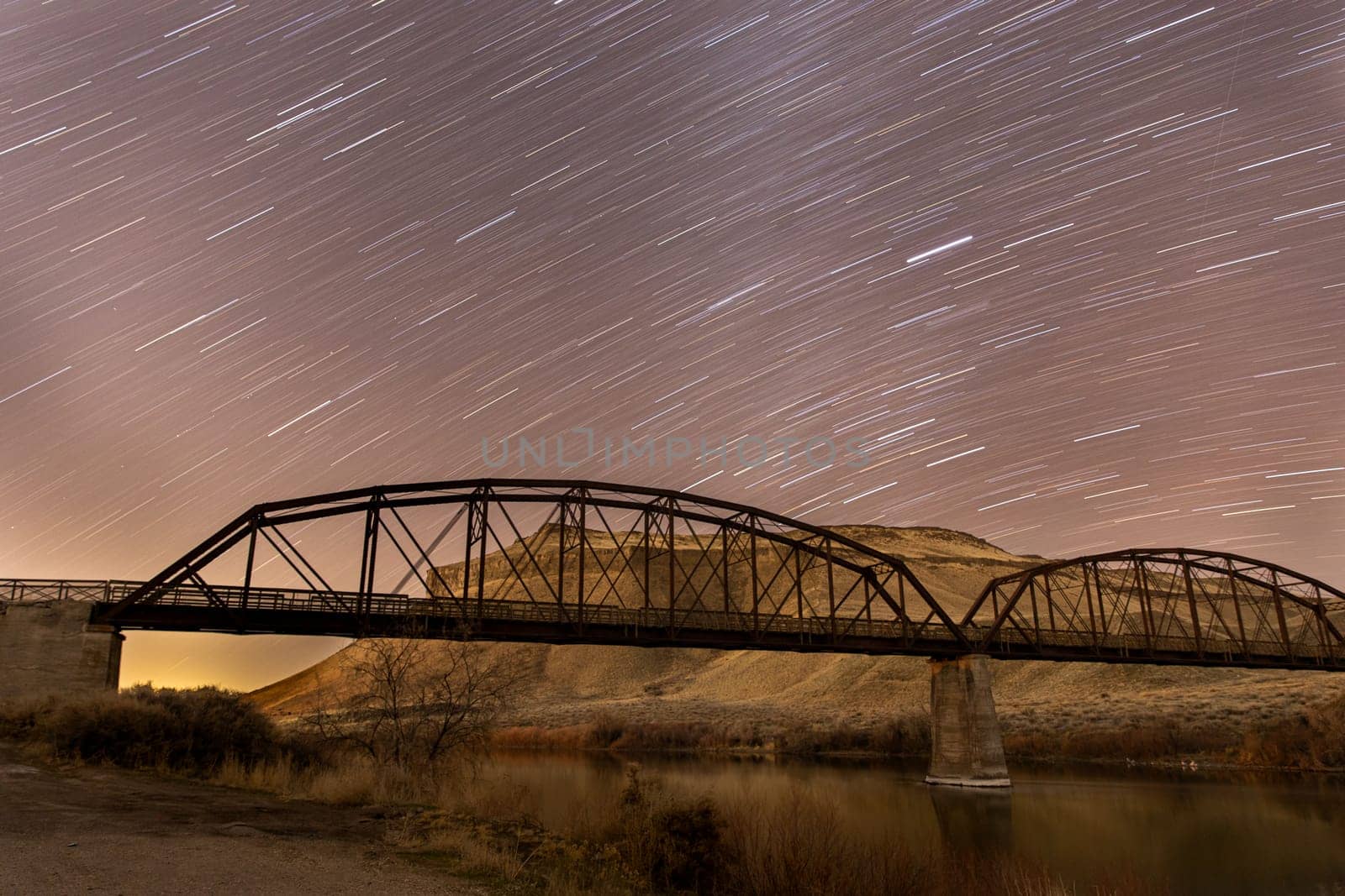 star trails on a bridge with the night sky lit up