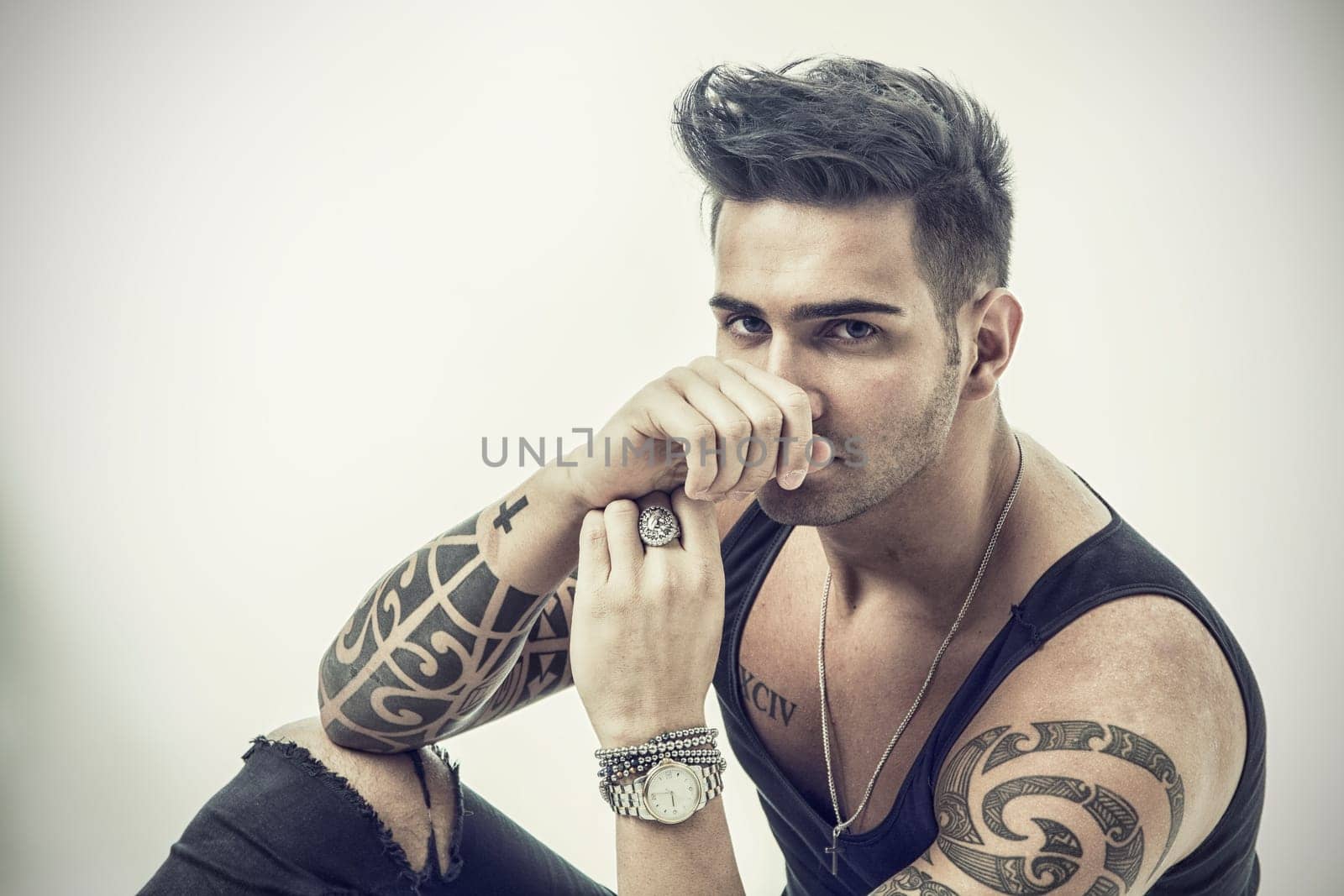 Handsome tattooed young man wearing grey t-shirt, sitting against grey background in studio shot