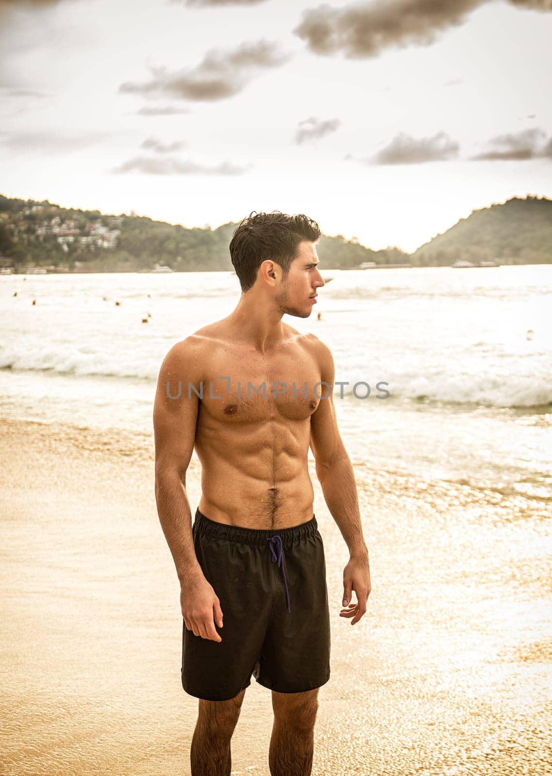 Attractive young man standing on a beach in Phuket Island, Thailand, shirtless wearing boxer shorts, showing muscular fit body