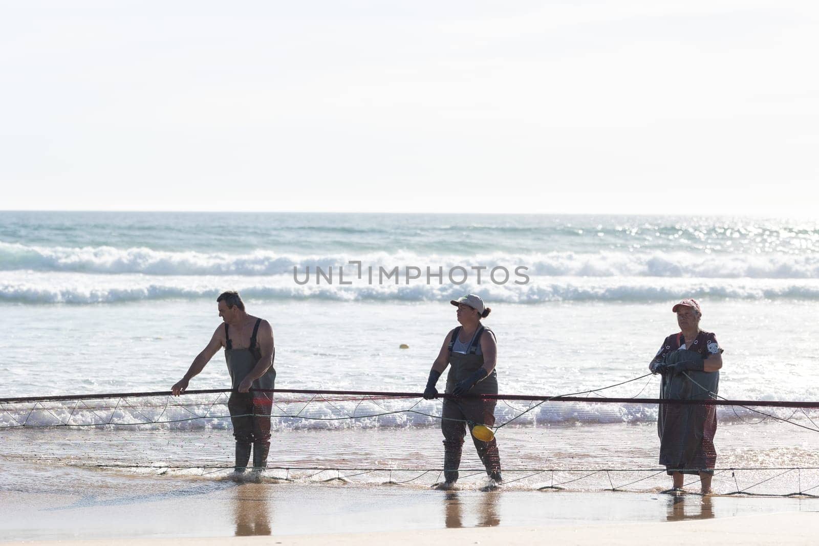 24 April 2023 Lisbon, Portugal: fishermen on the shore pull big fishing net out of the sea. Mid shot