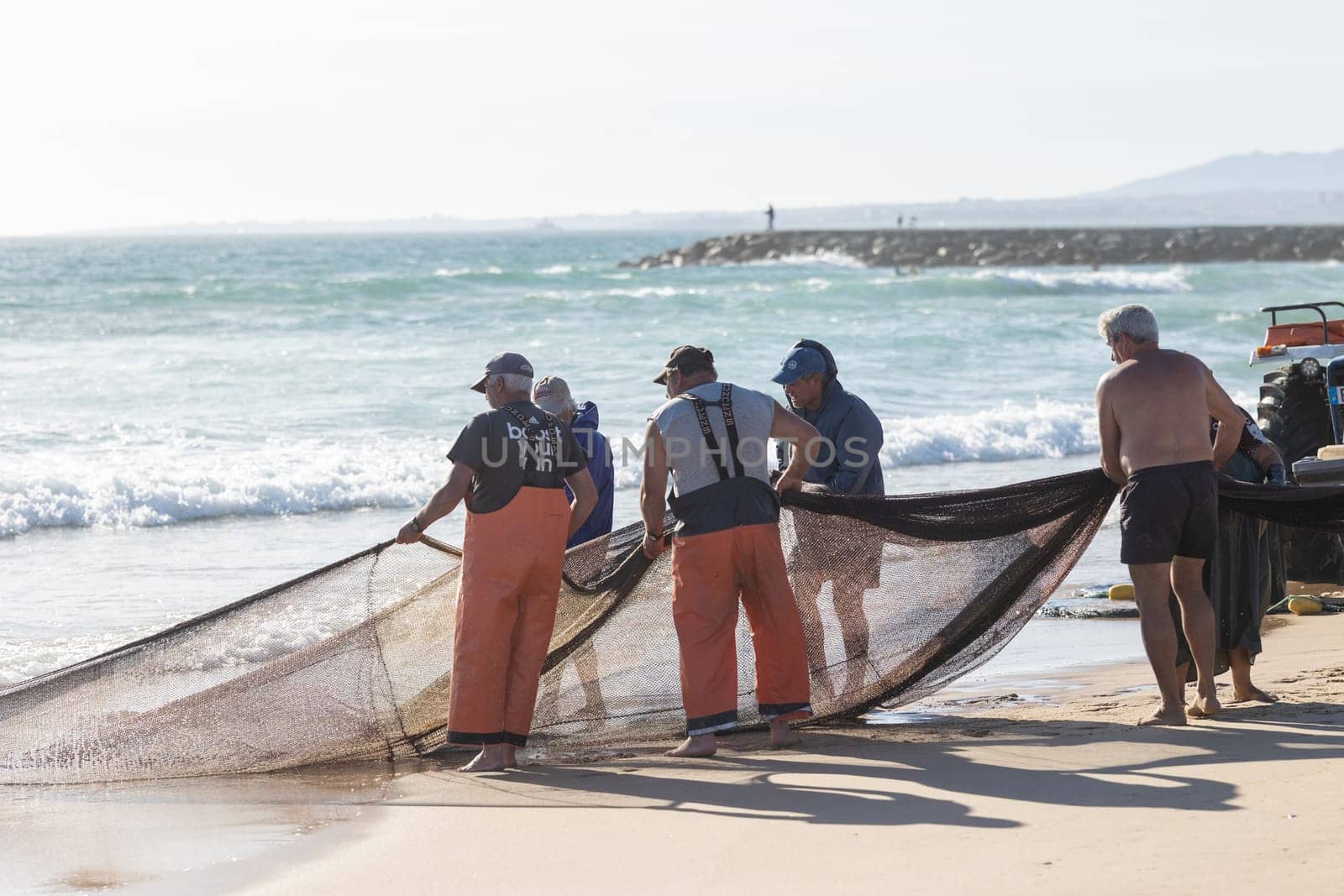 24 April 2023 Lisbon, Portugal: fishermen on the shore pull out fishing net out of the sea. Mid shot