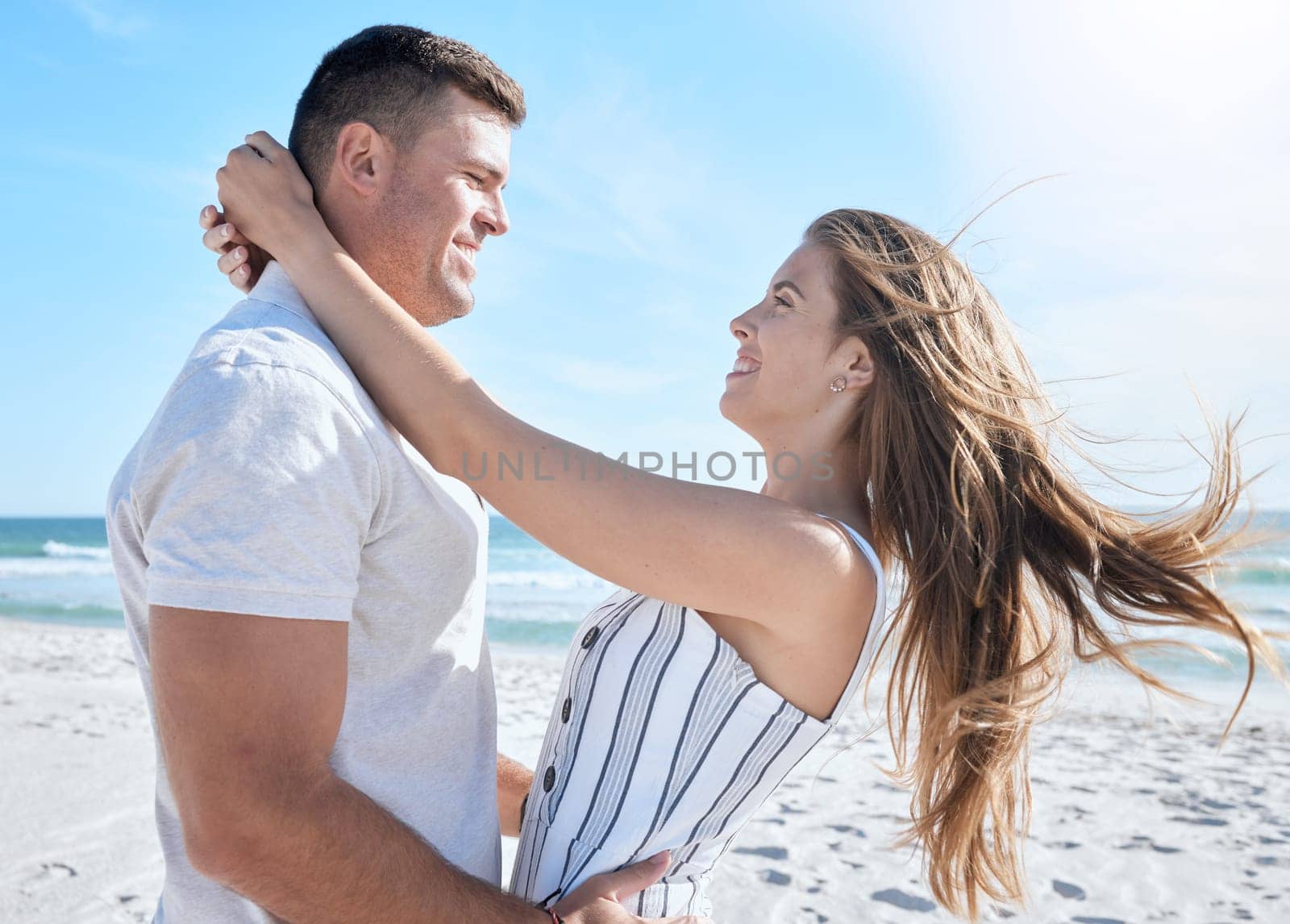 Love, beach and summer with a couple hugging on the sand by the sea or ocean while on holiday together. Happy, smile and romance with a man and woman bonding while on vacation or break by the water by YuriArcurs