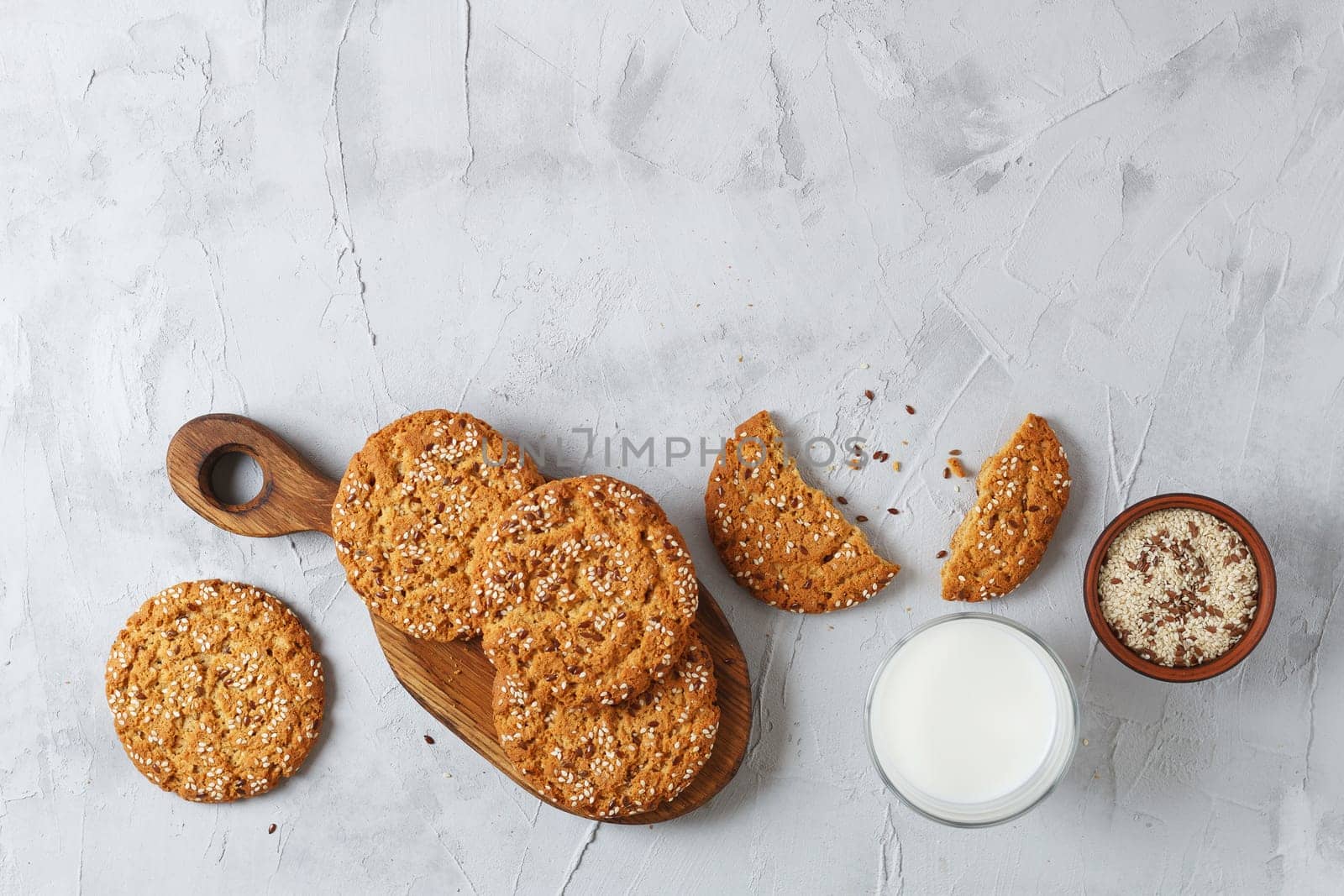 Oatmeal cookies with sesame seeds and flax seeds with a glass of milk on a gray background.Copy space