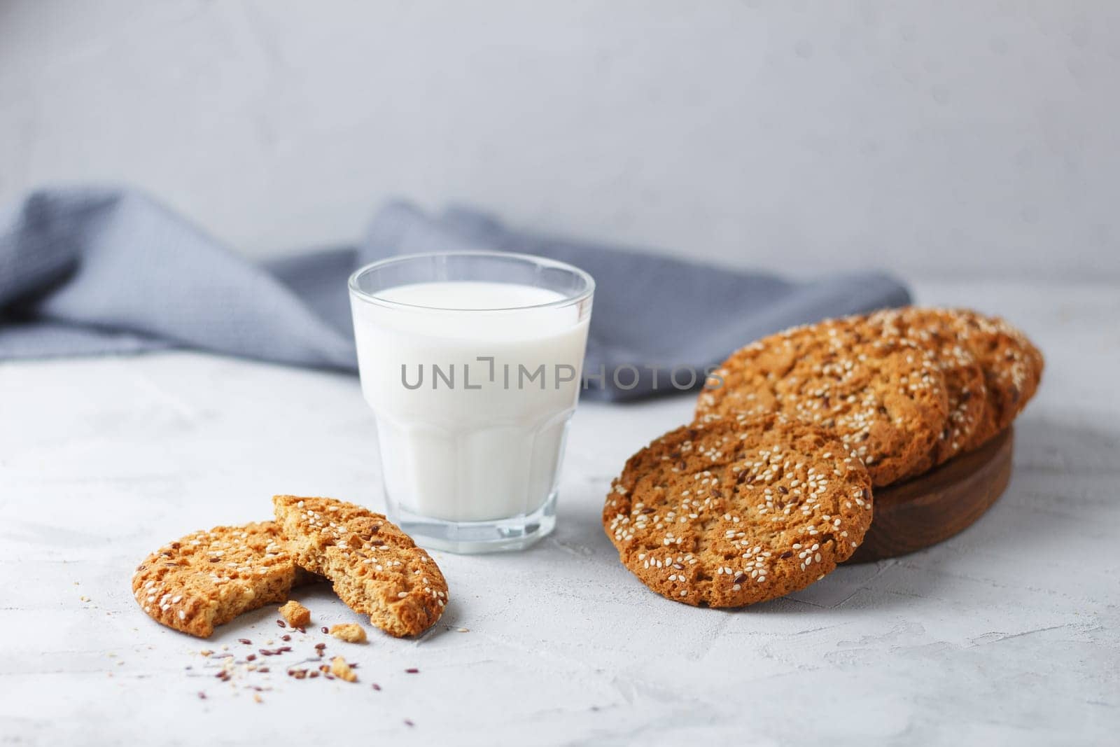 Oatmeal cookies with sesame seeds and flax seeds with a glass of milk on a gray background.