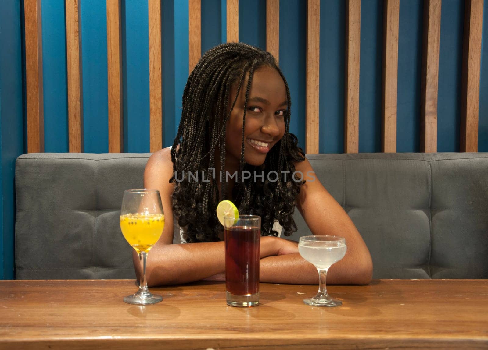 young afro man smiling at camera with three different cocktails on the table by Raulmartin