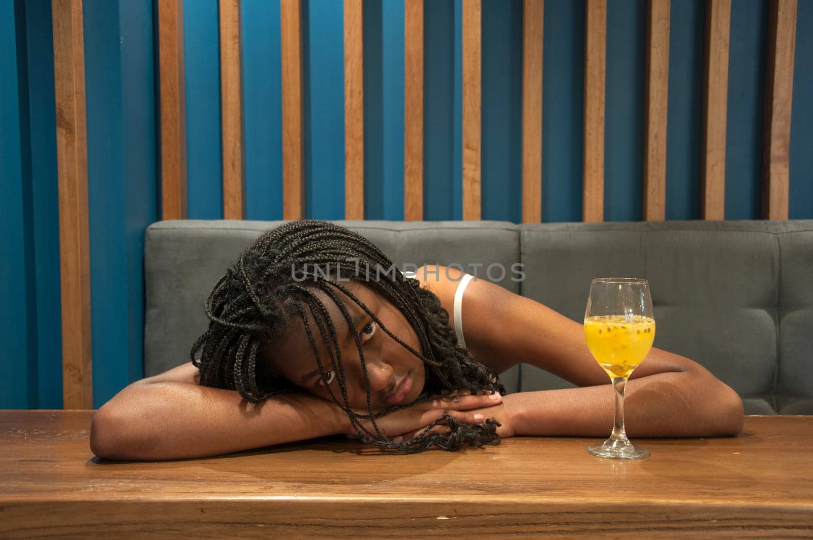 drunk afro girl on top of a table, looking at camera and a glass of alcohol next to her. High quality photo