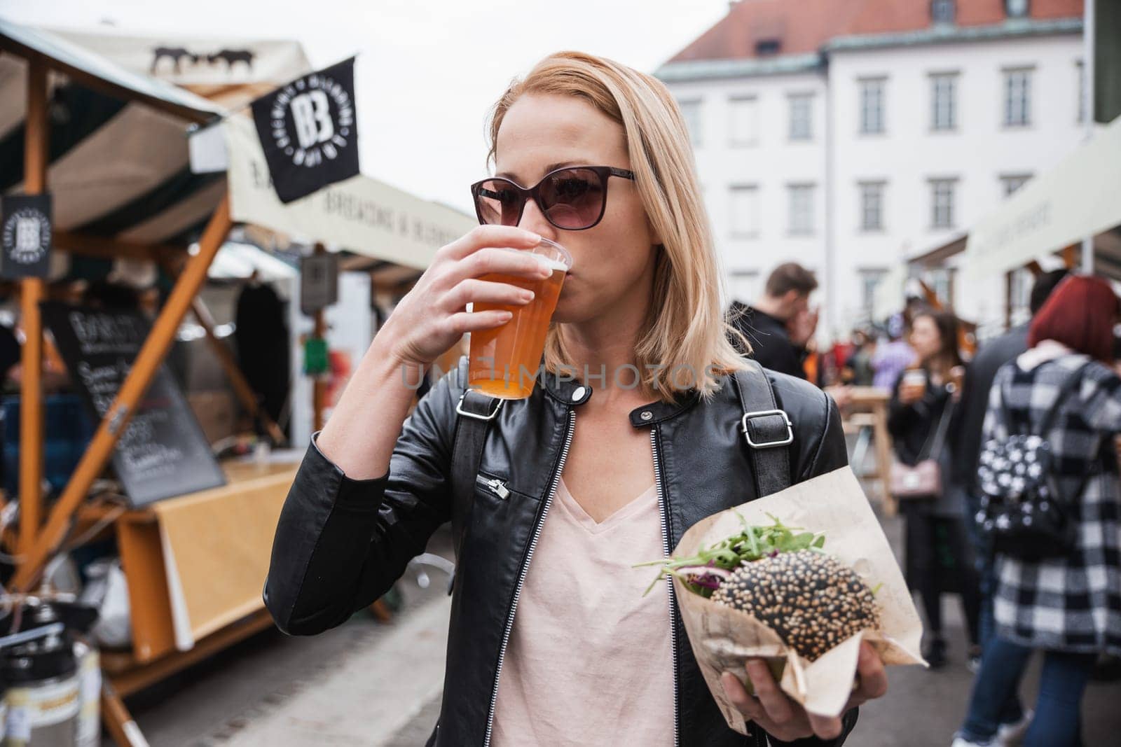 Beautiful young woman holding delicious organic salmon vegetarian burger and drinking homebrewed IPA beer on open air beer an burger urban street food festival in Ljubljana, Slovenia. by kasto