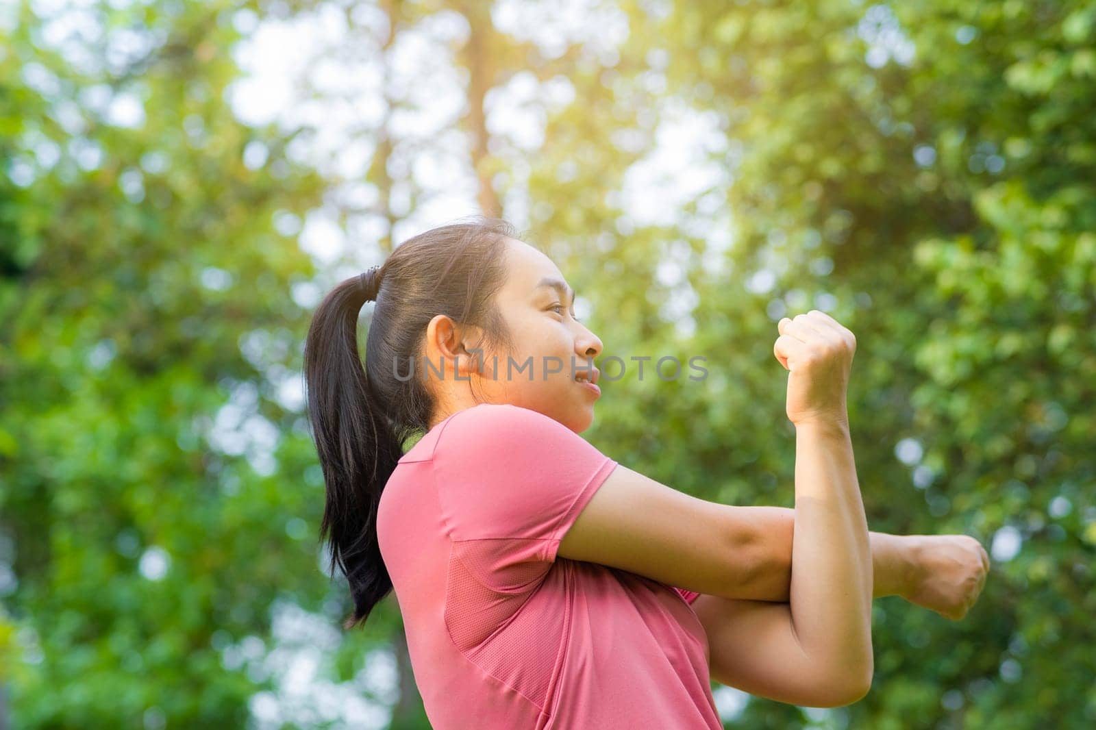 Young Asian woman in sportswear stretches before exercising in the park for a healthy lifestyle. Young healthy woman warming up outdoors. Healthy lifestyle concept. by TEERASAK