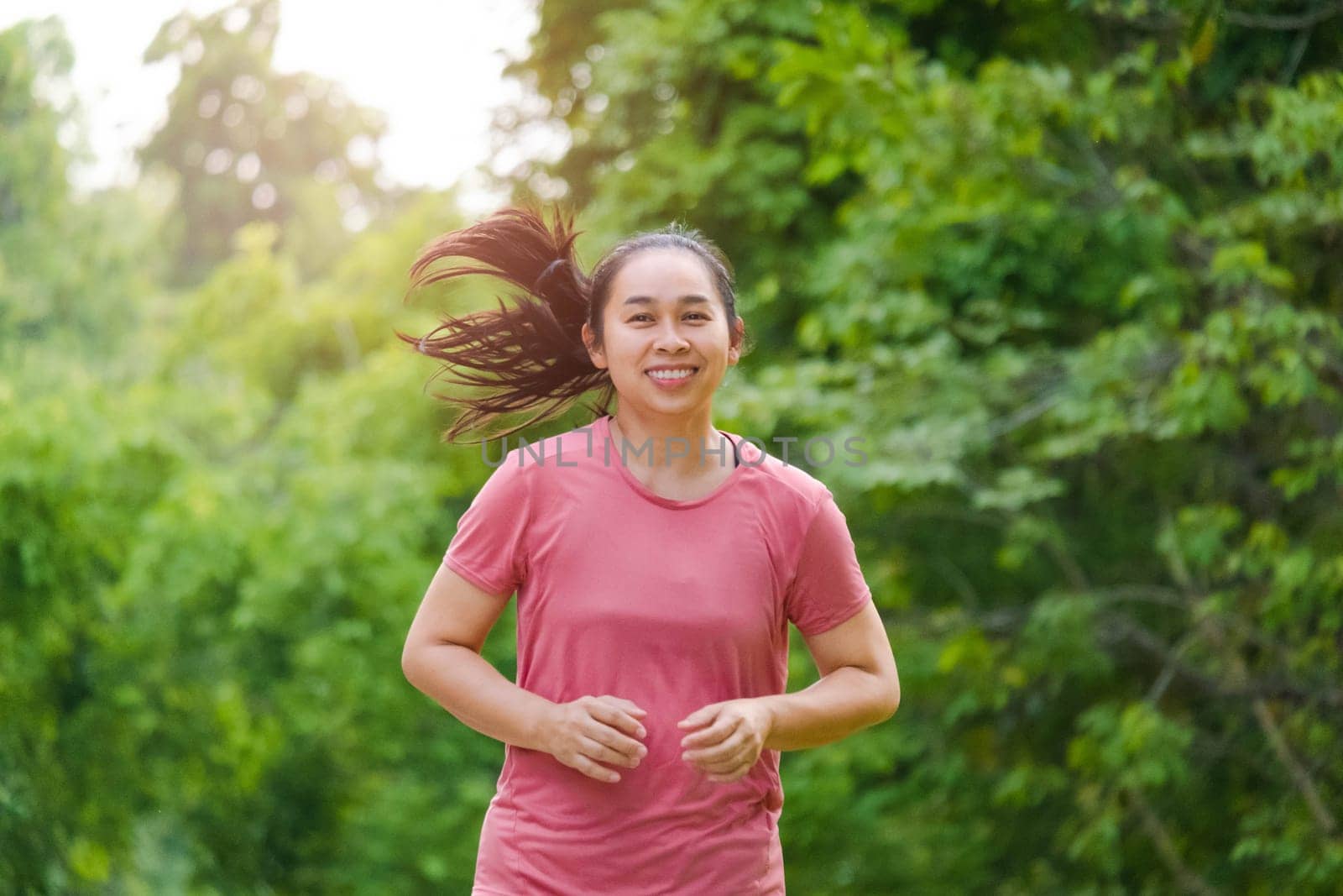 Woman jogging in the park in the sunshine on a beautiful summer day. Beautiful young woman jogging training exercise. Healthy lifestyle concept. by TEERASAK