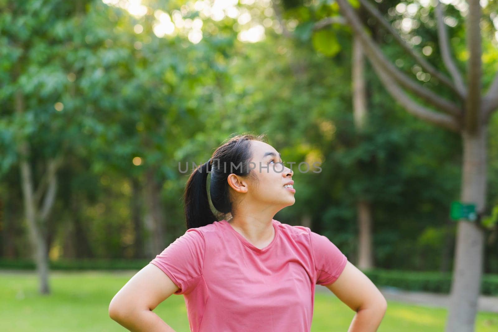 Portrait of young Asian woman in sportswear resting after jogging. Healthy young woman taking a break after jogging in the park. Healthy lifestyle concept.