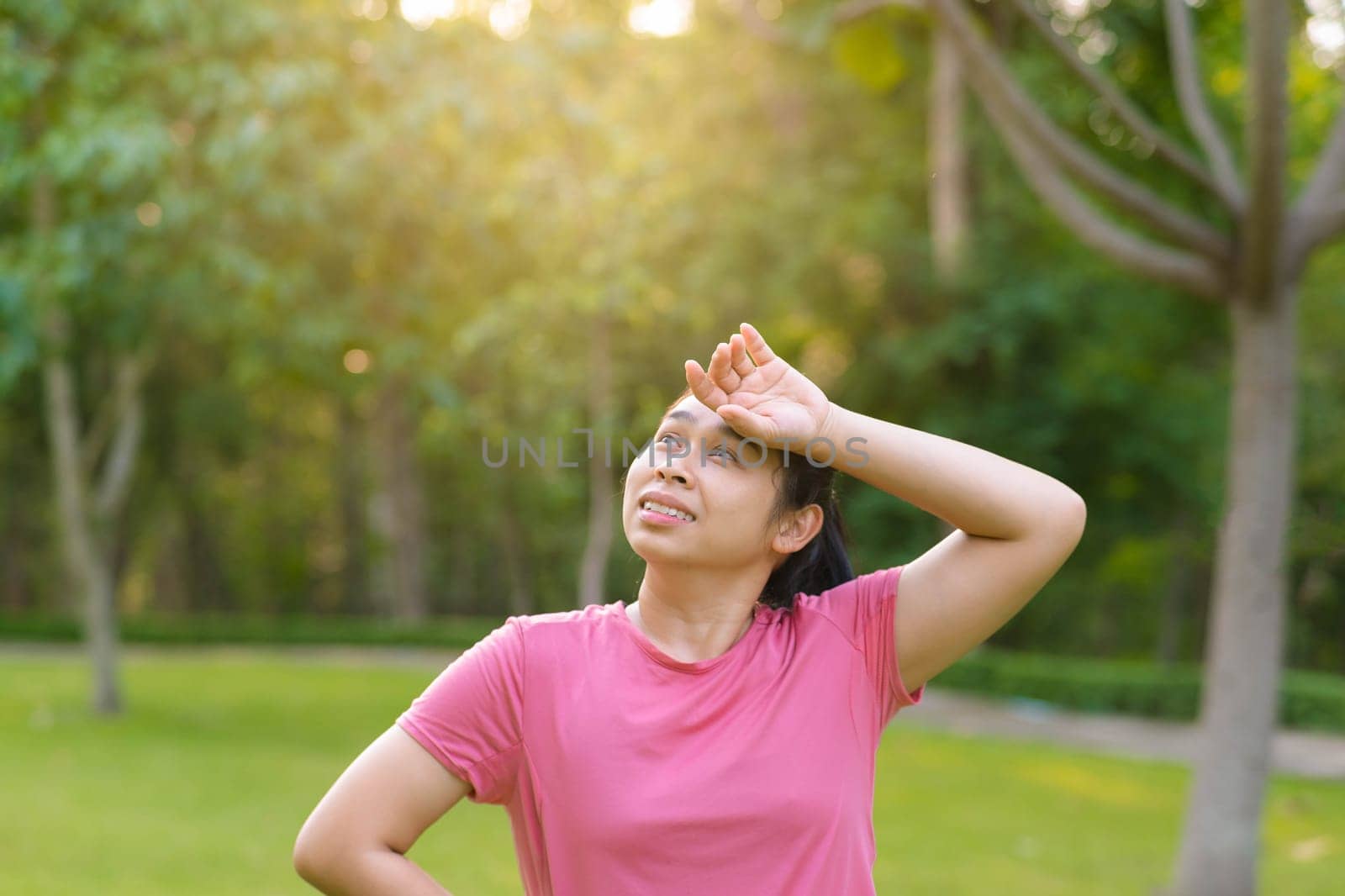 Portrait of young Asian woman in sportswear resting after jogging. Healthy young woman taking a break after jogging in the park. Healthy lifestyle concept. by TEERASAK
