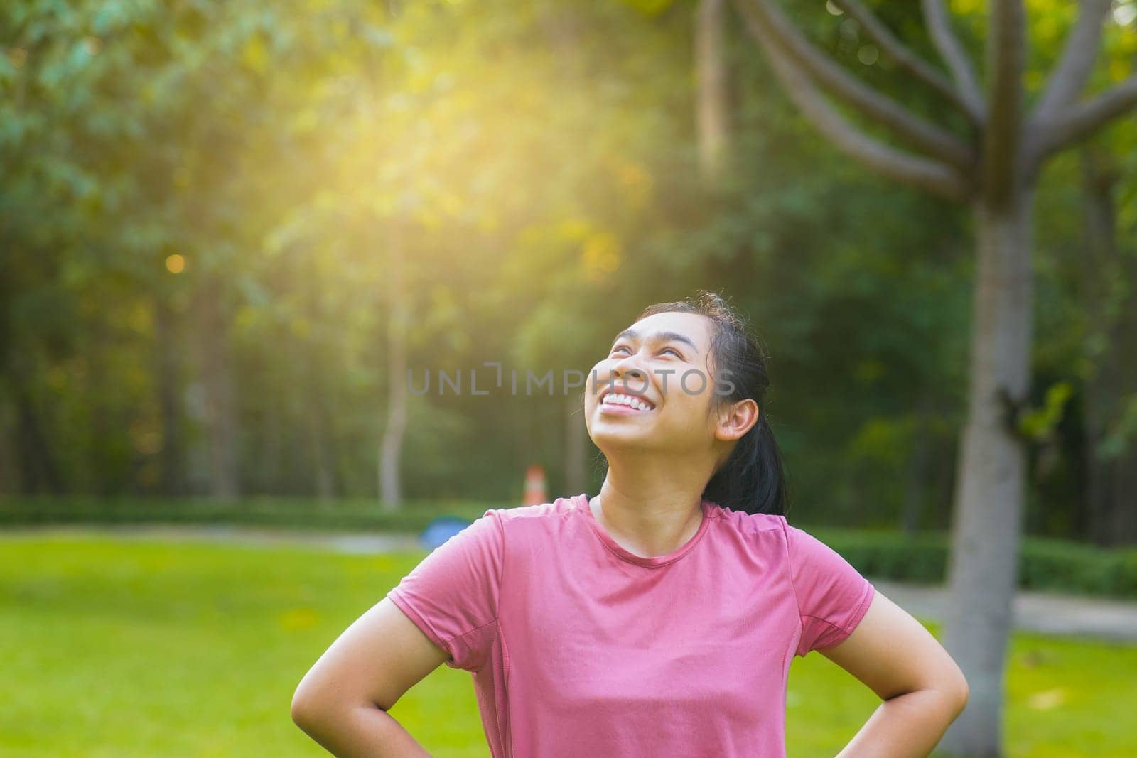 Portrait of young Asian woman in sportswear resting after jogging. Healthy young woman taking a break after jogging in the park. Healthy lifestyle concept. by TEERASAK