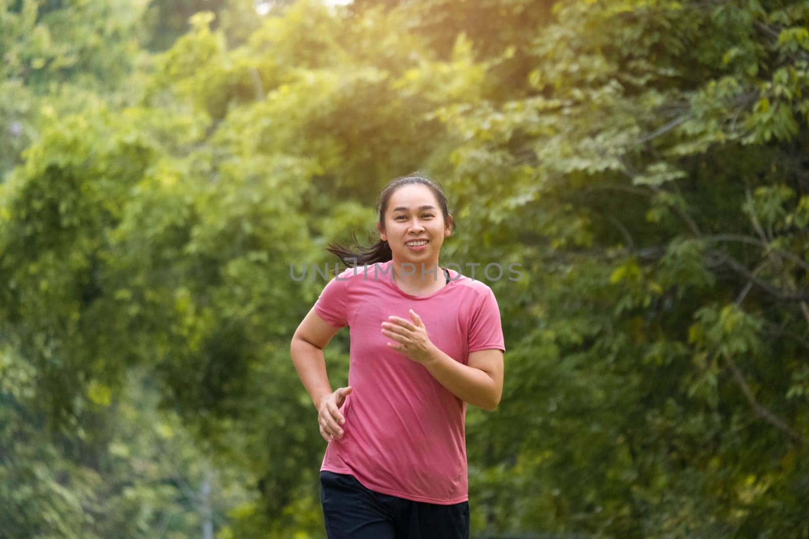 Woman jogging in the park in the sunshine on a beautiful summer day. Beautiful young woman jogging training exercise. Healthy lifestyle concept. by TEERASAK