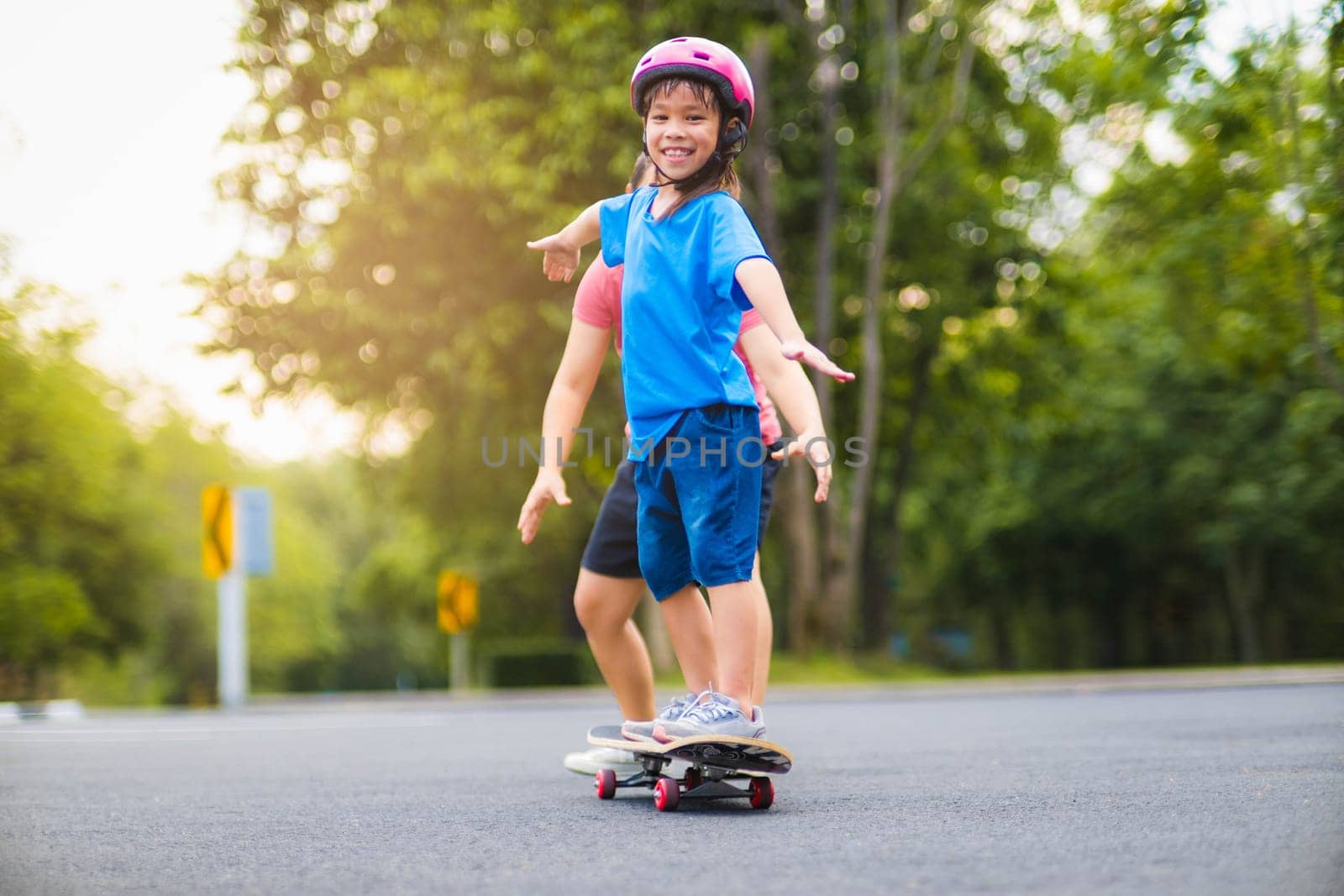 Active little girl and mom enjoy skateboarding. Cute little girl wearing helmet practicing skateboarding in park. Mother trains her daughter to skateboard. Outdoor sports for children.