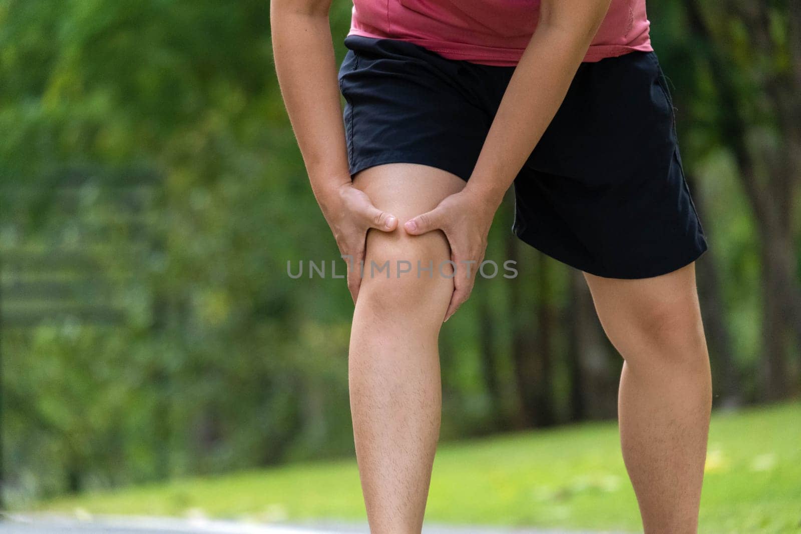 Close-up of young female athlete having knee pain after exercise. Female athlete having leg pain while exercising in park. Exercise injury concept by TEERASAK