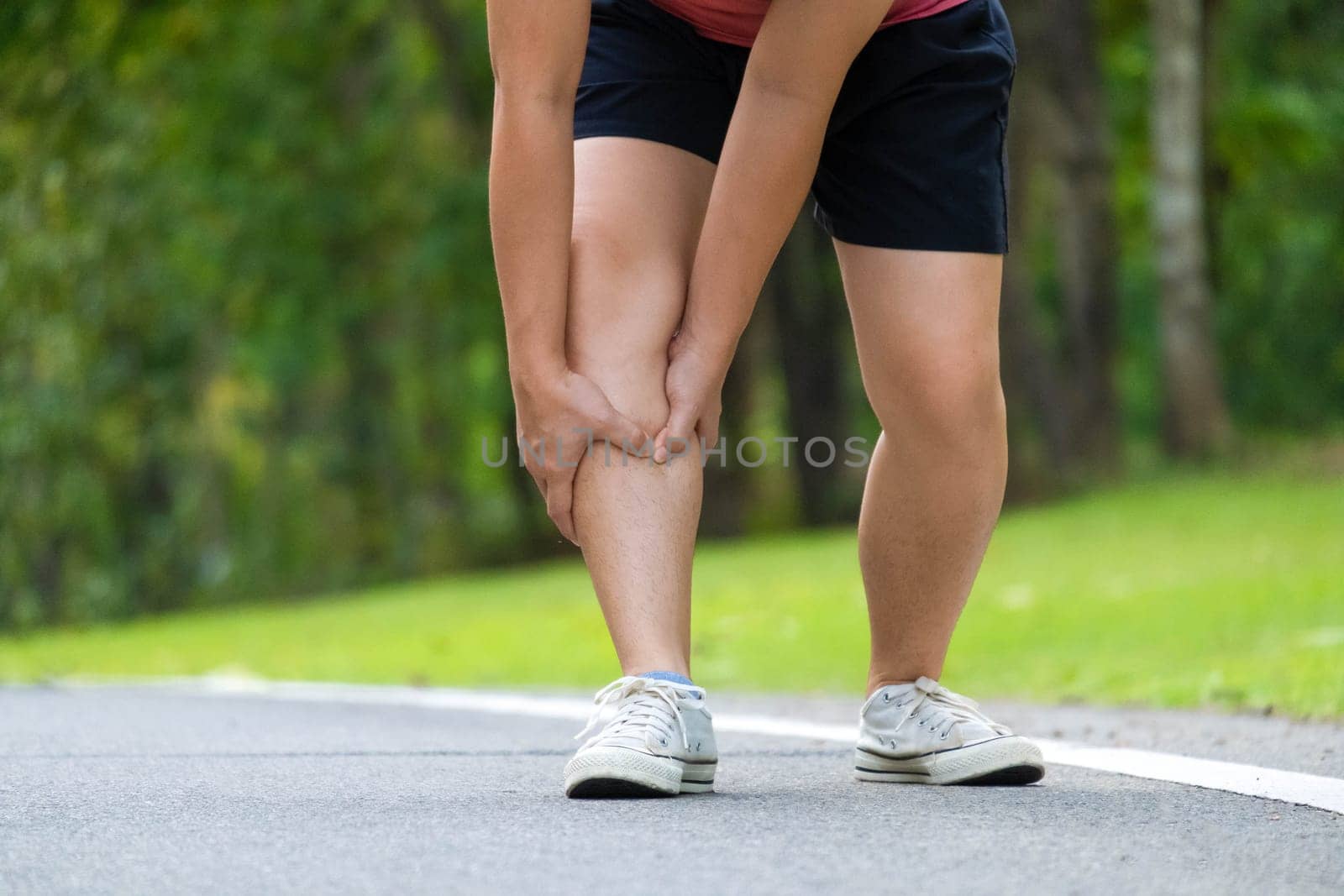 Close-up of young female athlete having knee pain after exercise. Female athlete having leg pain while exercising in park. Exercise injury concept by TEERASAK