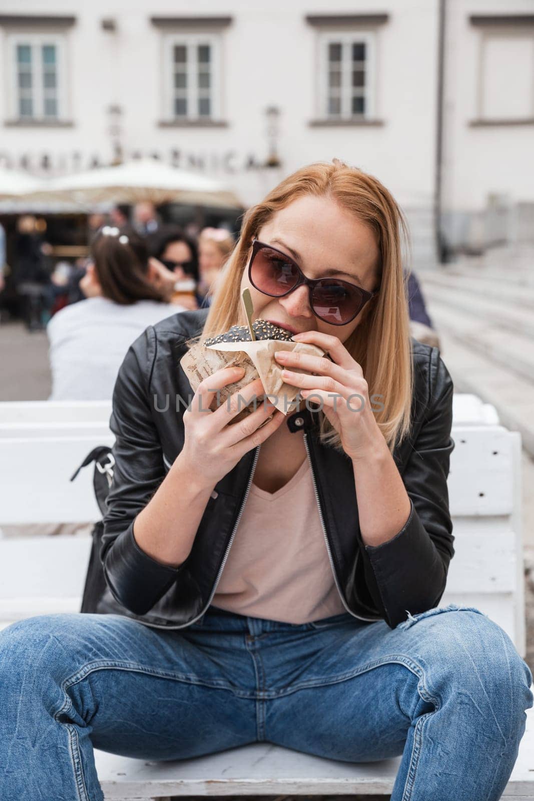 Pretty young blonde funny woman eating hamburger outdoor on the street. by kasto