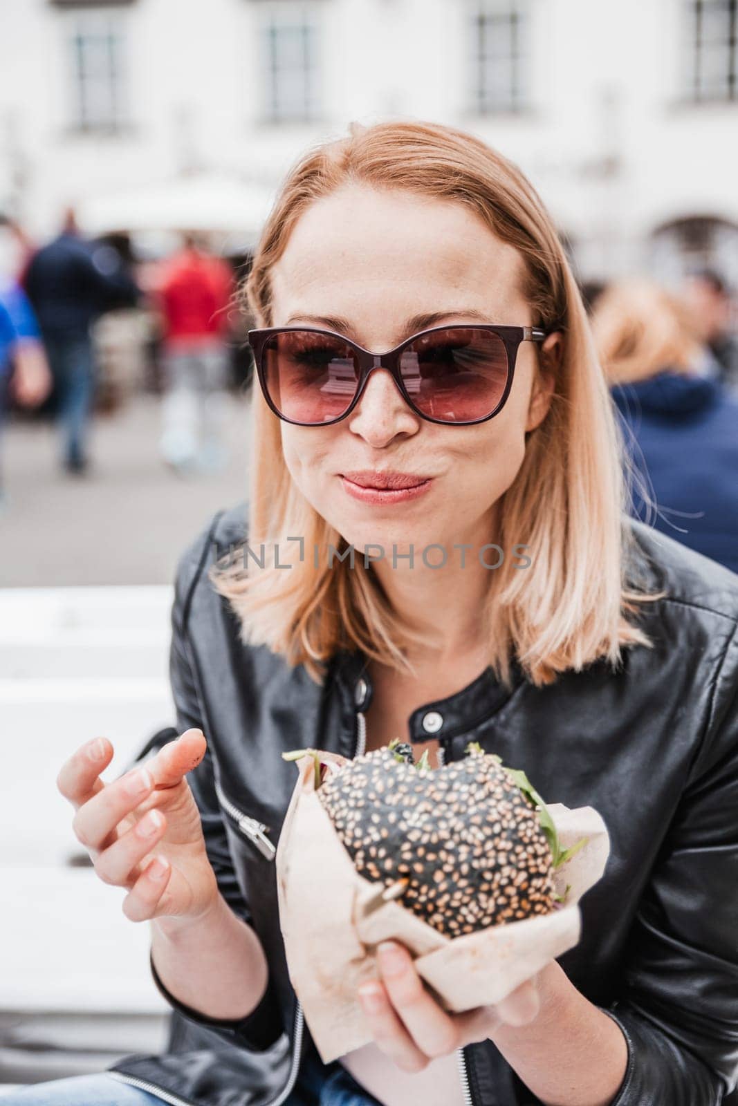 Pretty young blonde funny woman eating hamburger outdoor on the street. by kasto