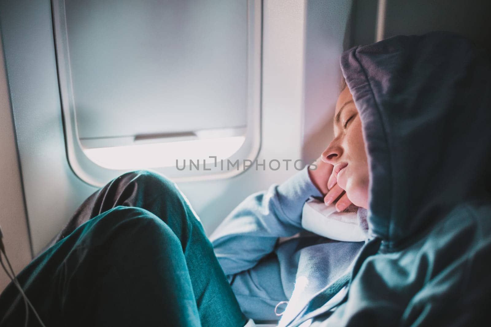 Tired blonde casual caucasian woman wearing sporty hoodie napping on seat while traveling by airplane. Commercial transportation by planes. Authentic image of real people. by kasto