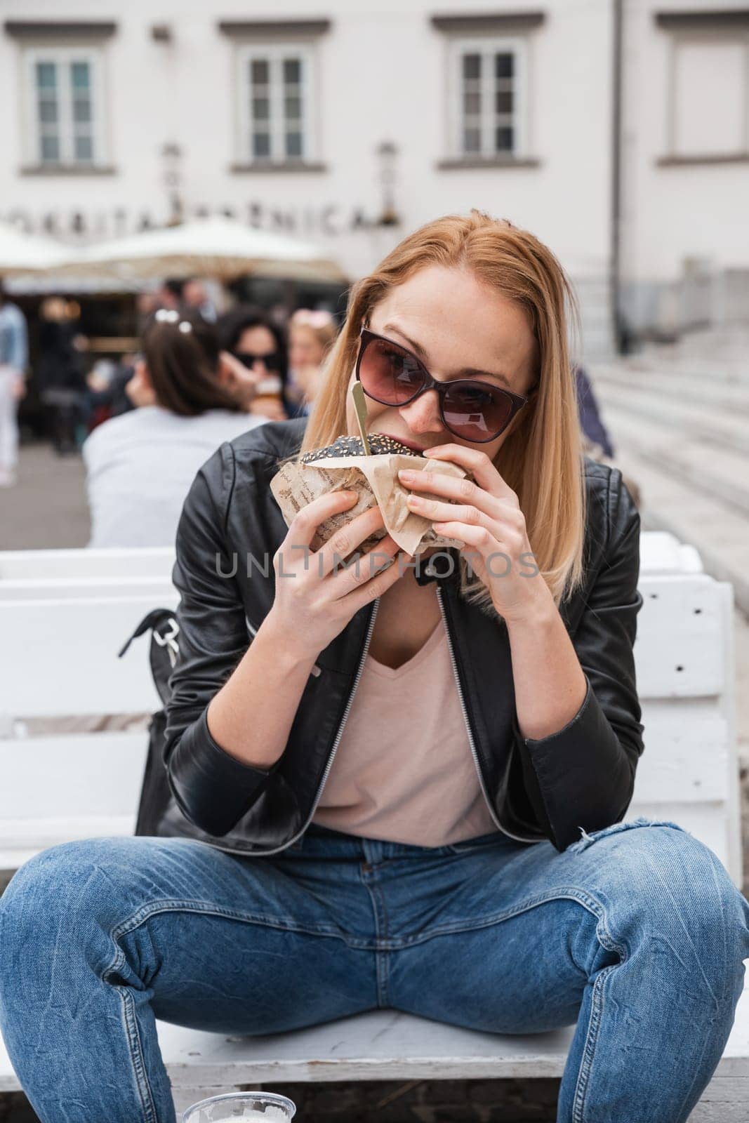 Pretty young blonde funny woman eating hamburger outdoor on the street