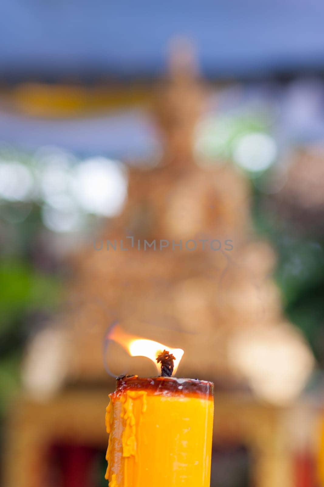 Candlelight burning in front of Buddha statue. Focus on candle frame, buddha blured in background