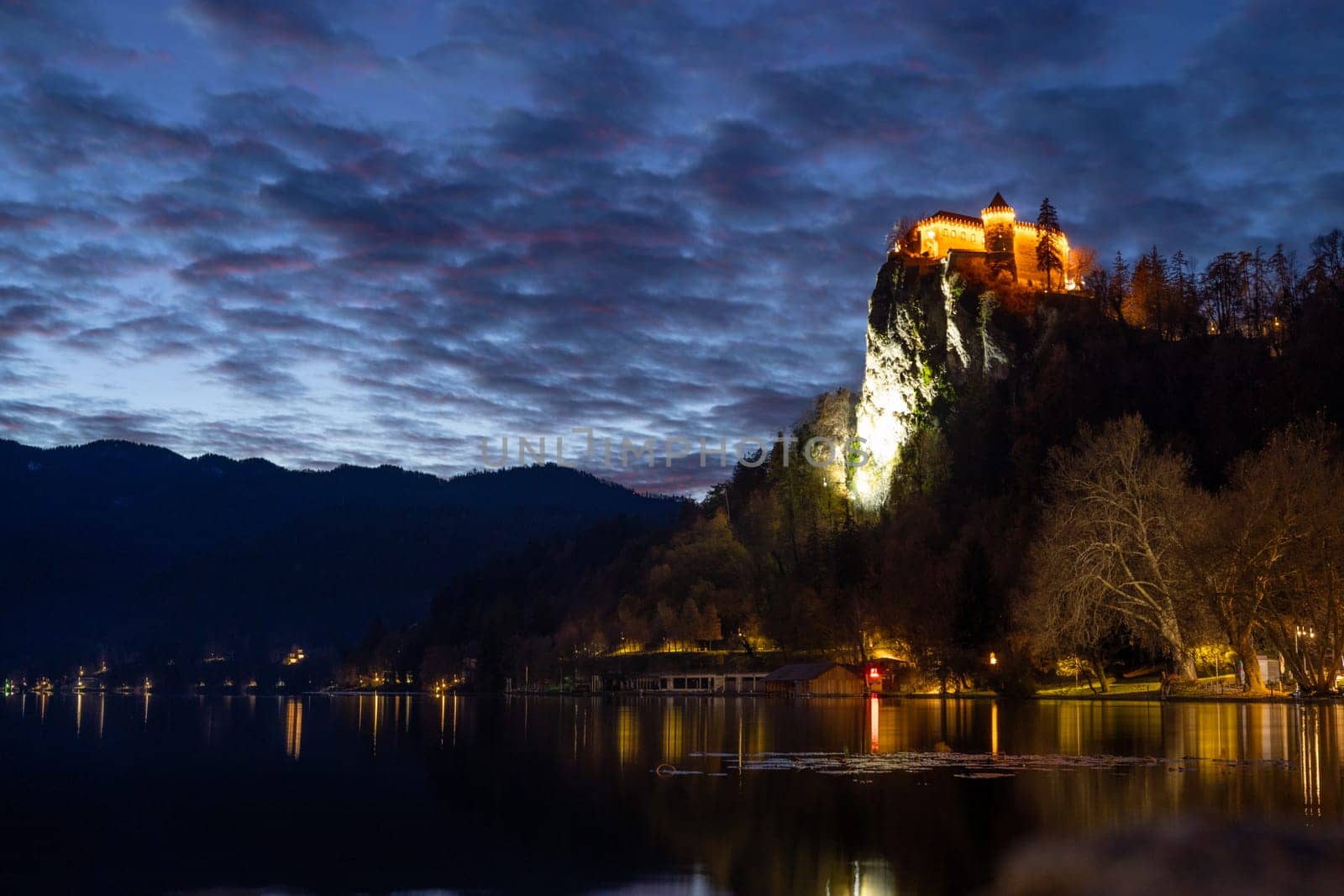 Dramatic cloudscape over medieval castle of Bled perched on cliff above Bled lake at dusk, Slovenia