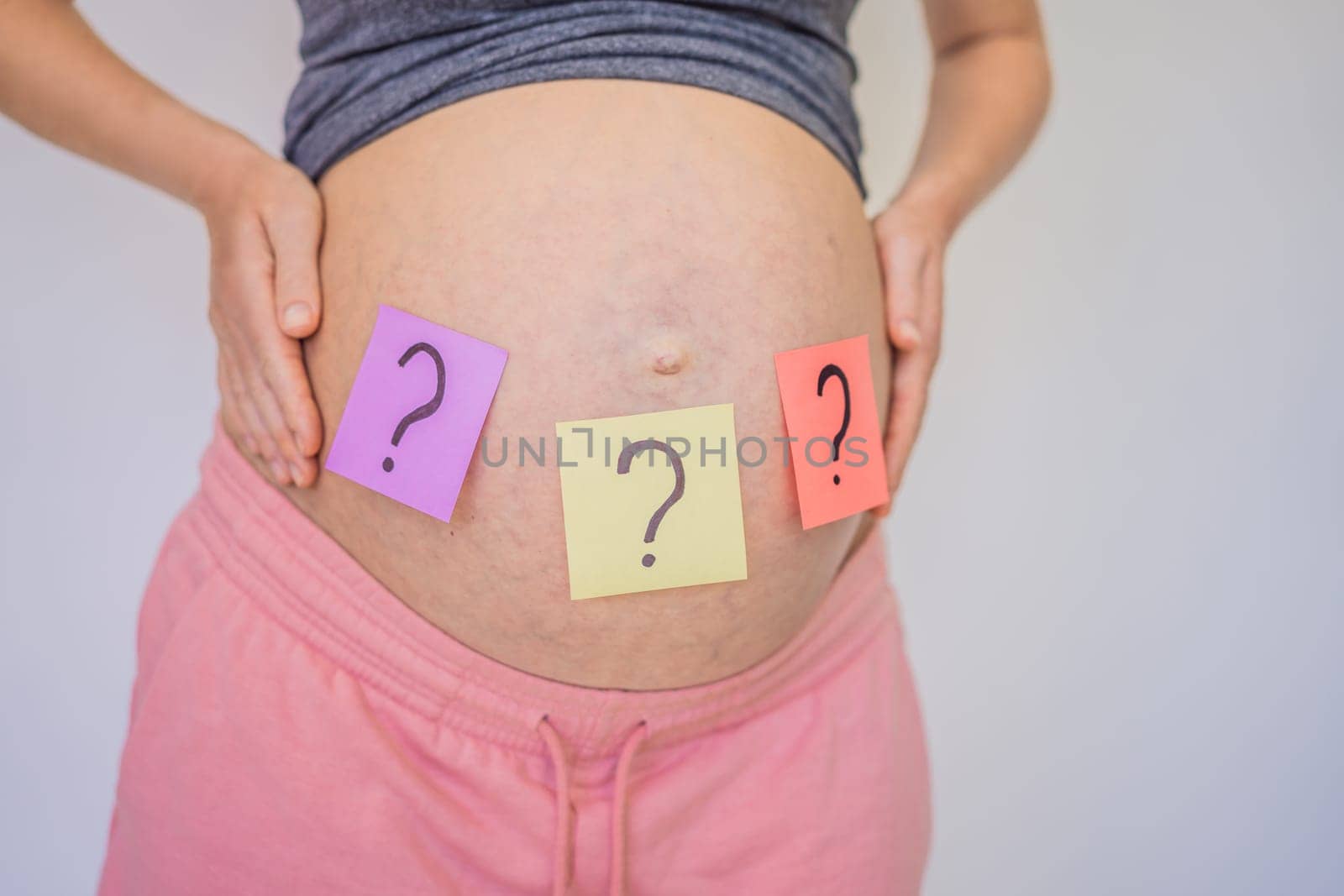 Choosing baby name. Confused pregnant woman with question marks on paper stickers on tummy.