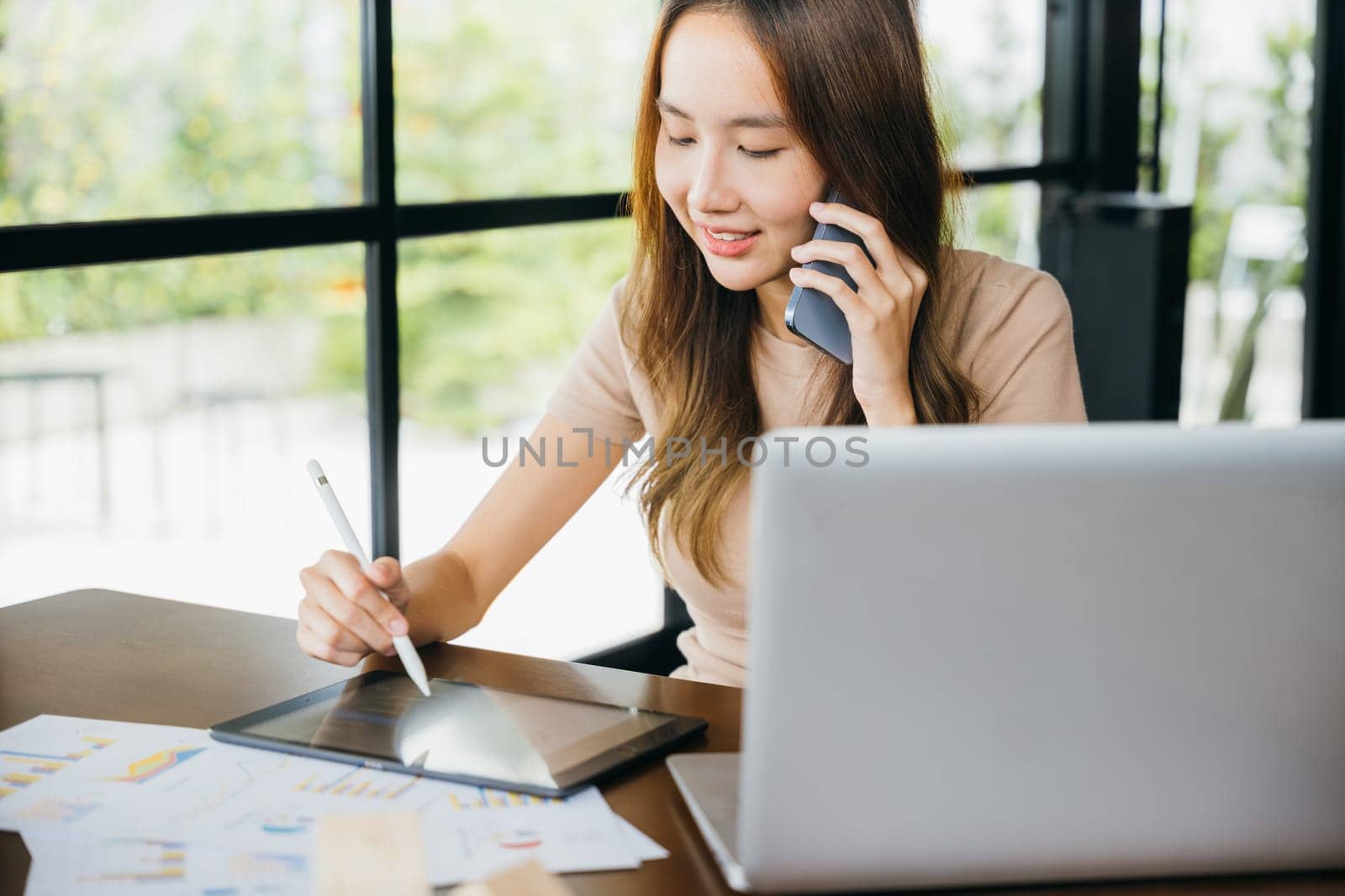 Asian Student female learning online course, business woman multitasking while talking on cellphone by smart mobile phone and writing taking notes on digital tablet computer in home office