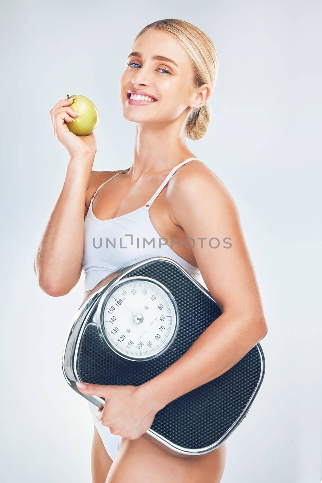 Health, diet and woman with scale and apple to lose weight for health, wellness and healthy lifestyle as fitness mockup studio background. Portrait, smile and body of model eating fruit for nutrition by YuriArcurs