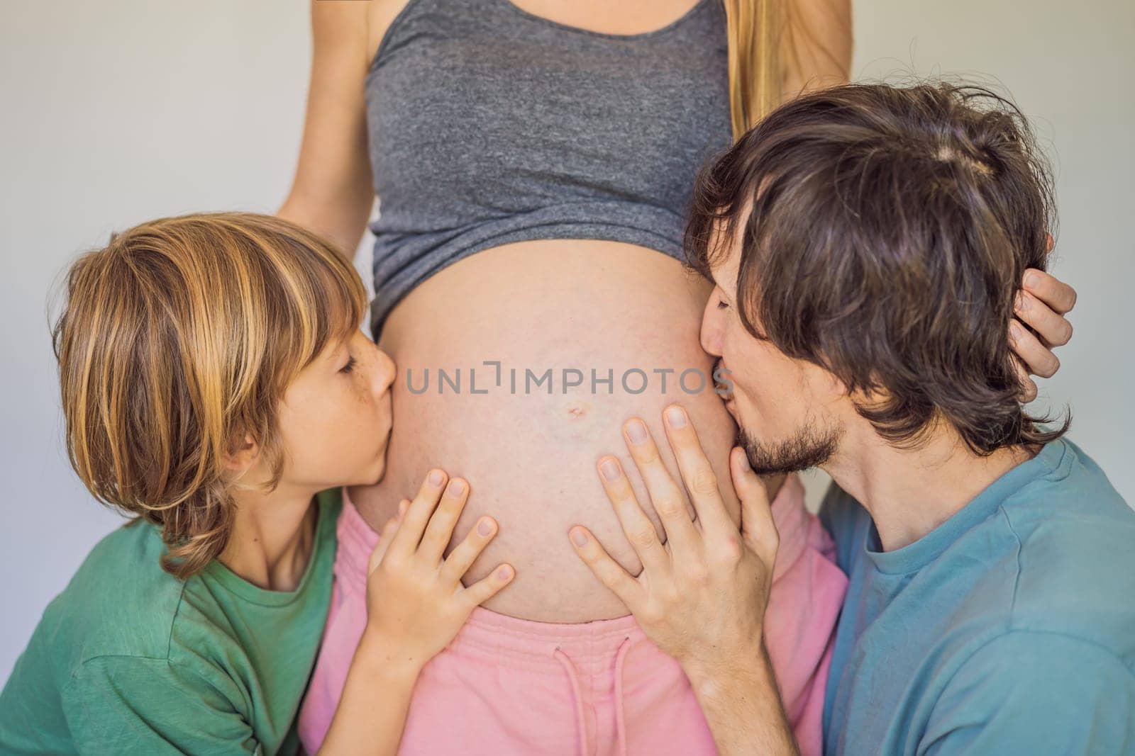 Father and elder son listen to mom's pregnant belly.