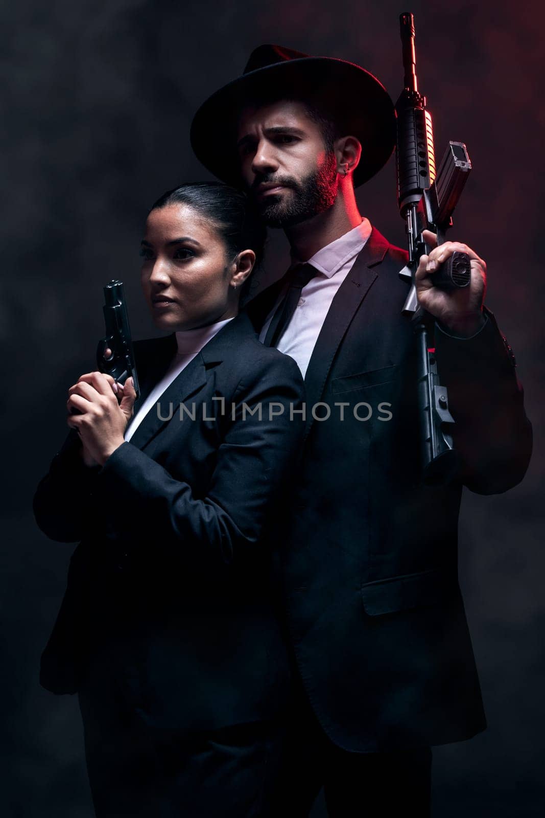 Gangster couple, fashion or gun on studio background in secret spy, isolated mafia safety or crime lord security. Man, love or model woman with pistol in stylish, trendy or fashion clothes aesthetic by YuriArcurs