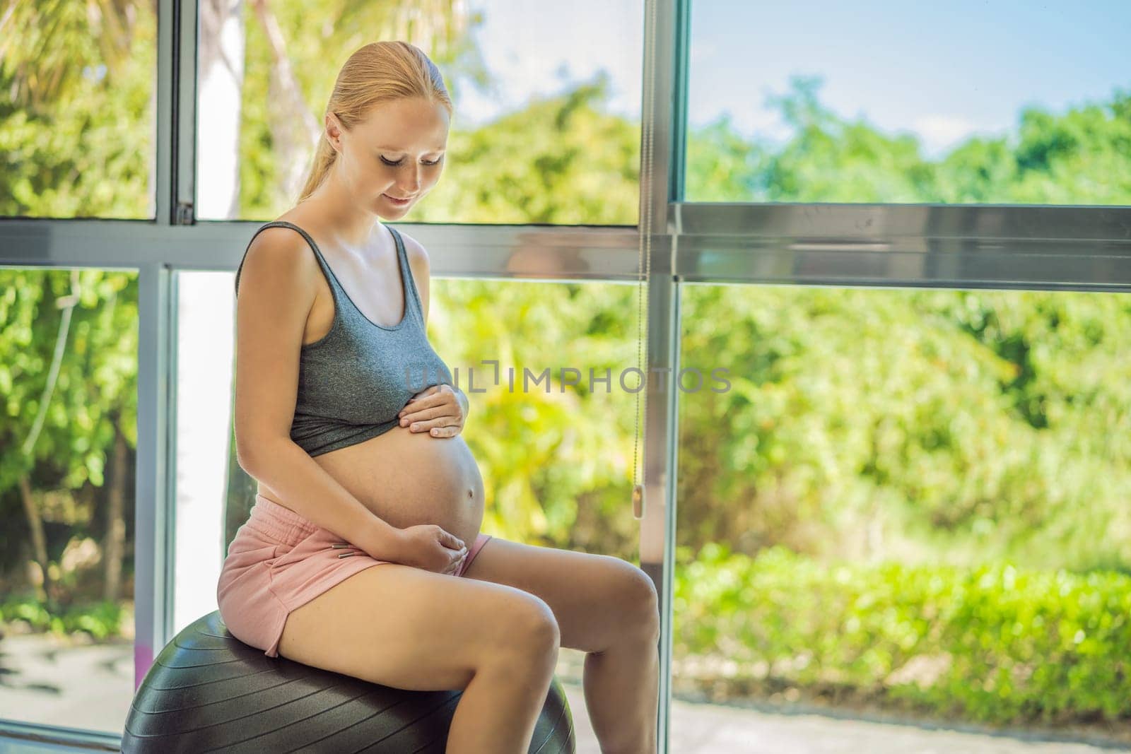 Pregnant woman exercising on fitball at home. Pregnant woman doing relax exercises with a fitness pilates ball. Against the background of the window.