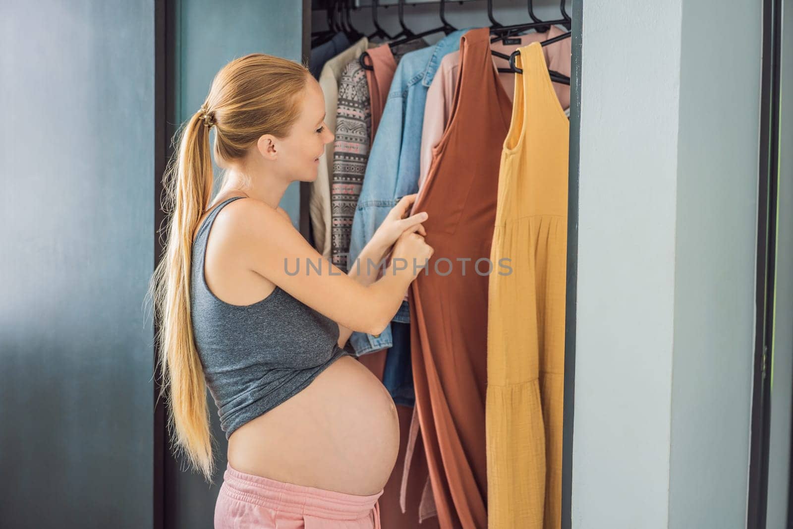 A pregnant woman has nothing to wear. A pregnant woman stands in front of a closet with clothes and does not know what to wear because the clothes do not fit on her.
