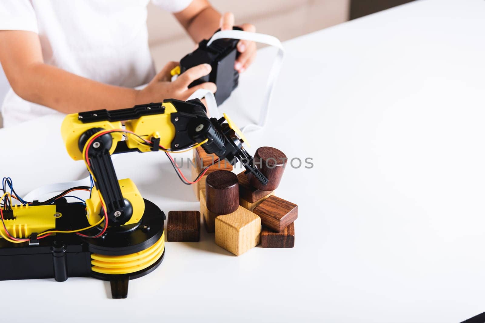 Happy Asian little kid boy using remote control playing robotic machine arm for pick up wood block by Sorapop