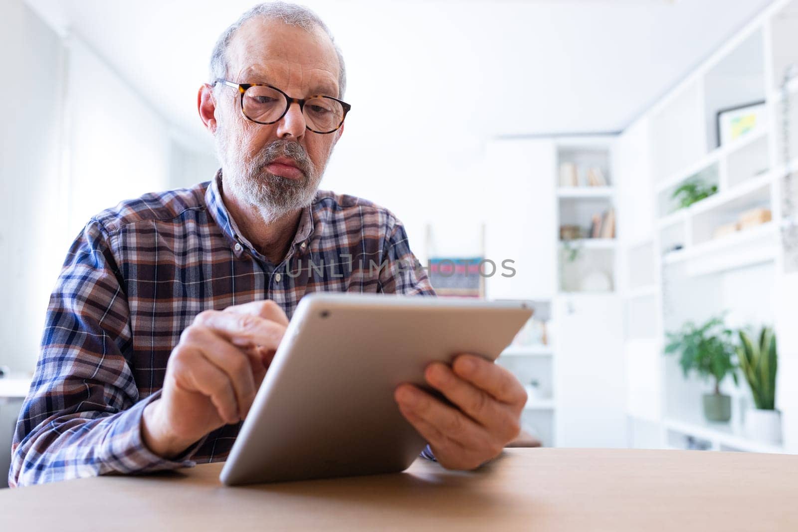 Senior caucasian man with glasses using digital tablet at home. Copy space. by Hoverstock