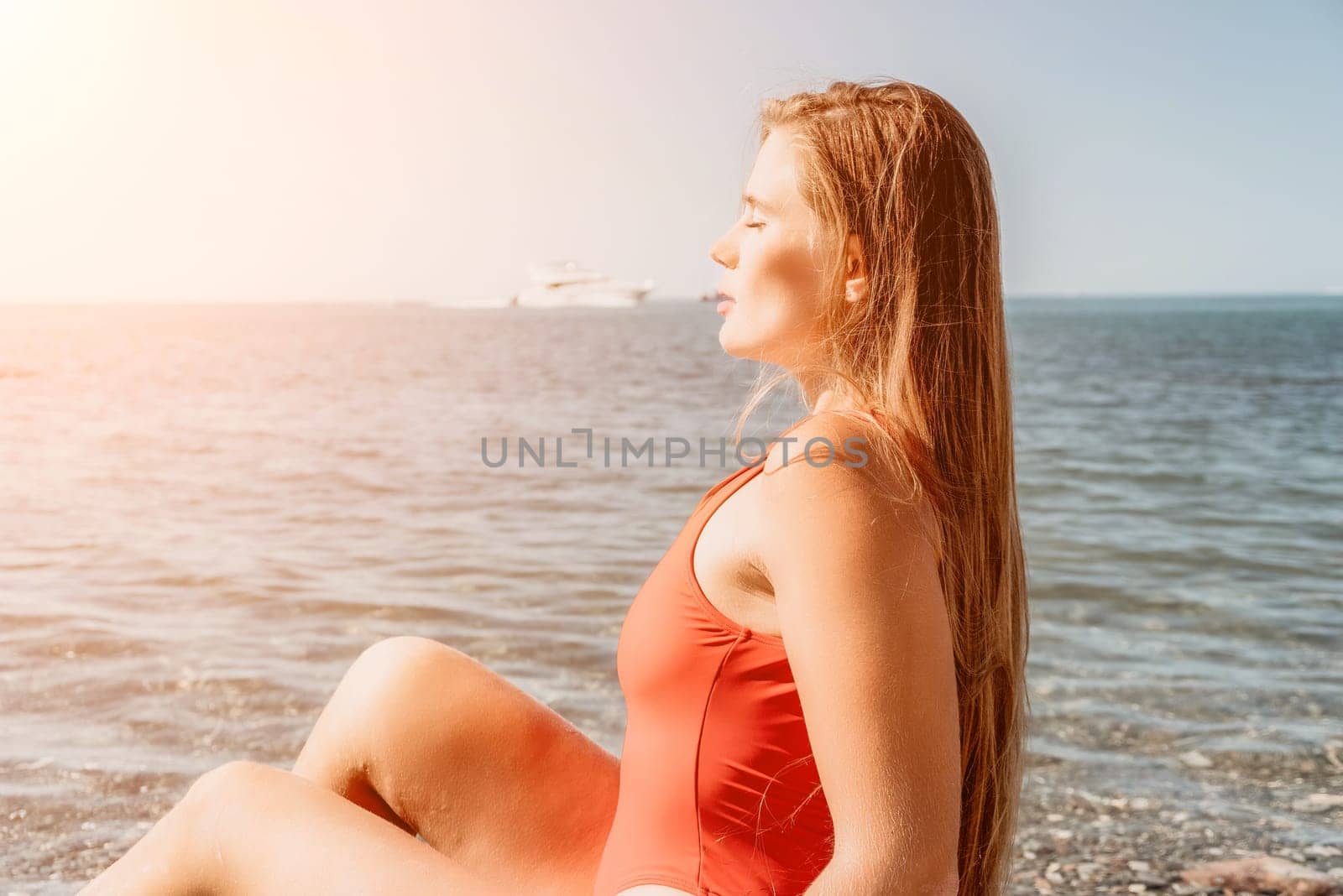 Young woman in red bikini on Beach. Girl lying on pebble beach and enjoying sun. Happy lady with long hair in bathing suit chilling and sunbathing by turquoise sea ocean on hot summer day. Close up by panophotograph