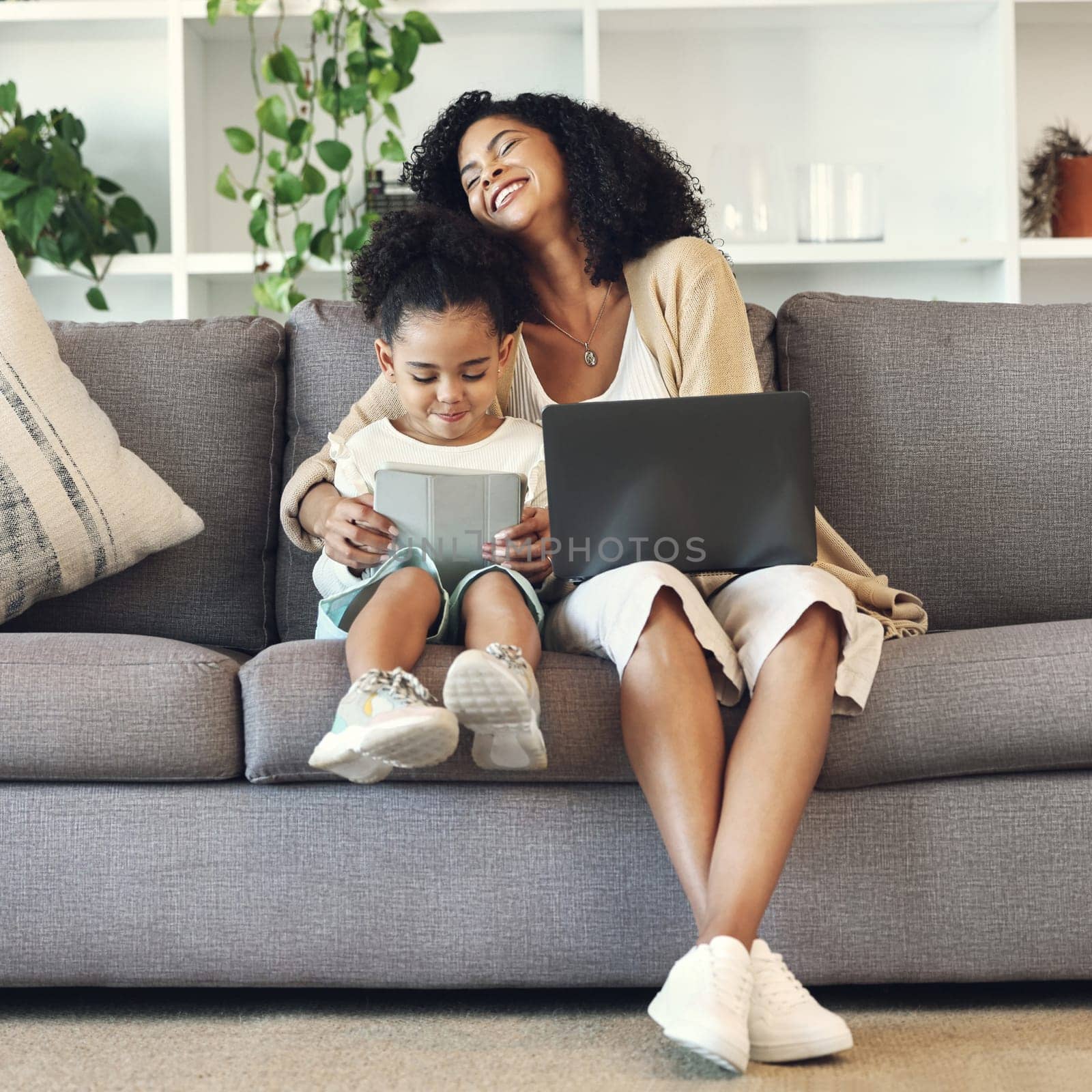 Mother, child and technology in family home living room for remote work, online education and wifi. Woman laugh and girl with laptop and table on couch for internet learning, game and funny movies by YuriArcurs
