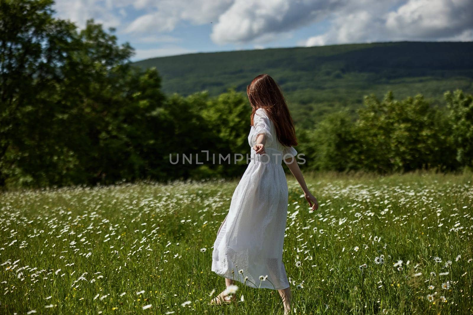 a free woman in a light dress runs through a field of daisies with her back to the camera. High quality photo