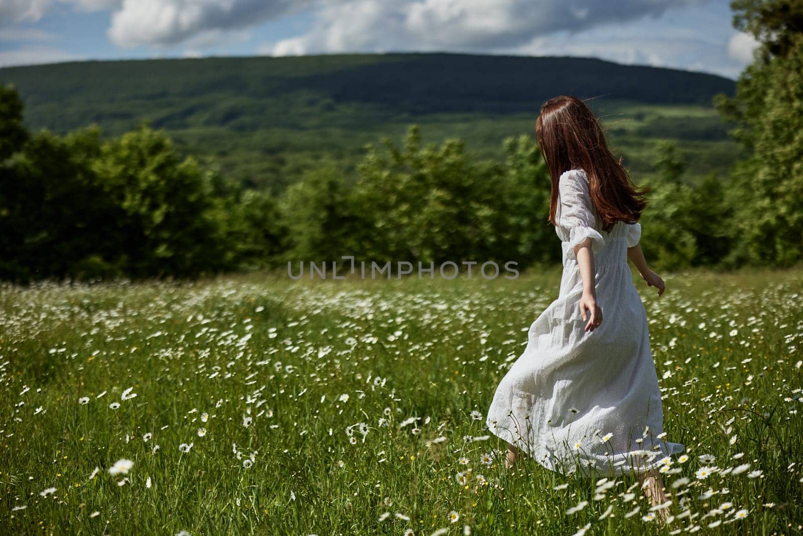 a free woman in a light dress runs through a field of daisies with her back to the camera by Vichizh