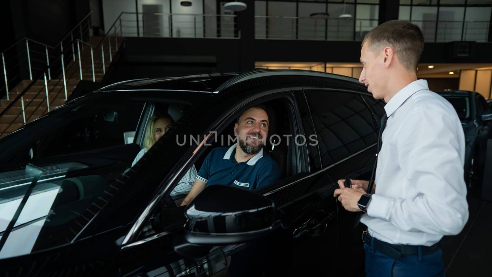 The seller demonstrates the interior of the car to buyers. Caucasian couple chooses a car. by mrwed54