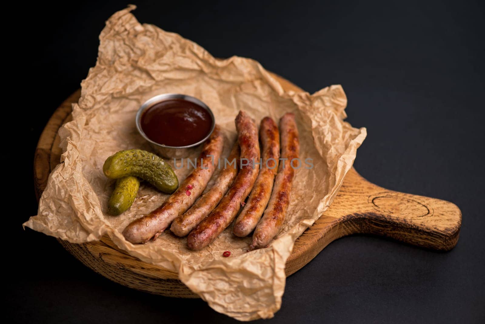 beer snacks - grilled sausages with sauce on a wooden board on a black background by aprilphoto