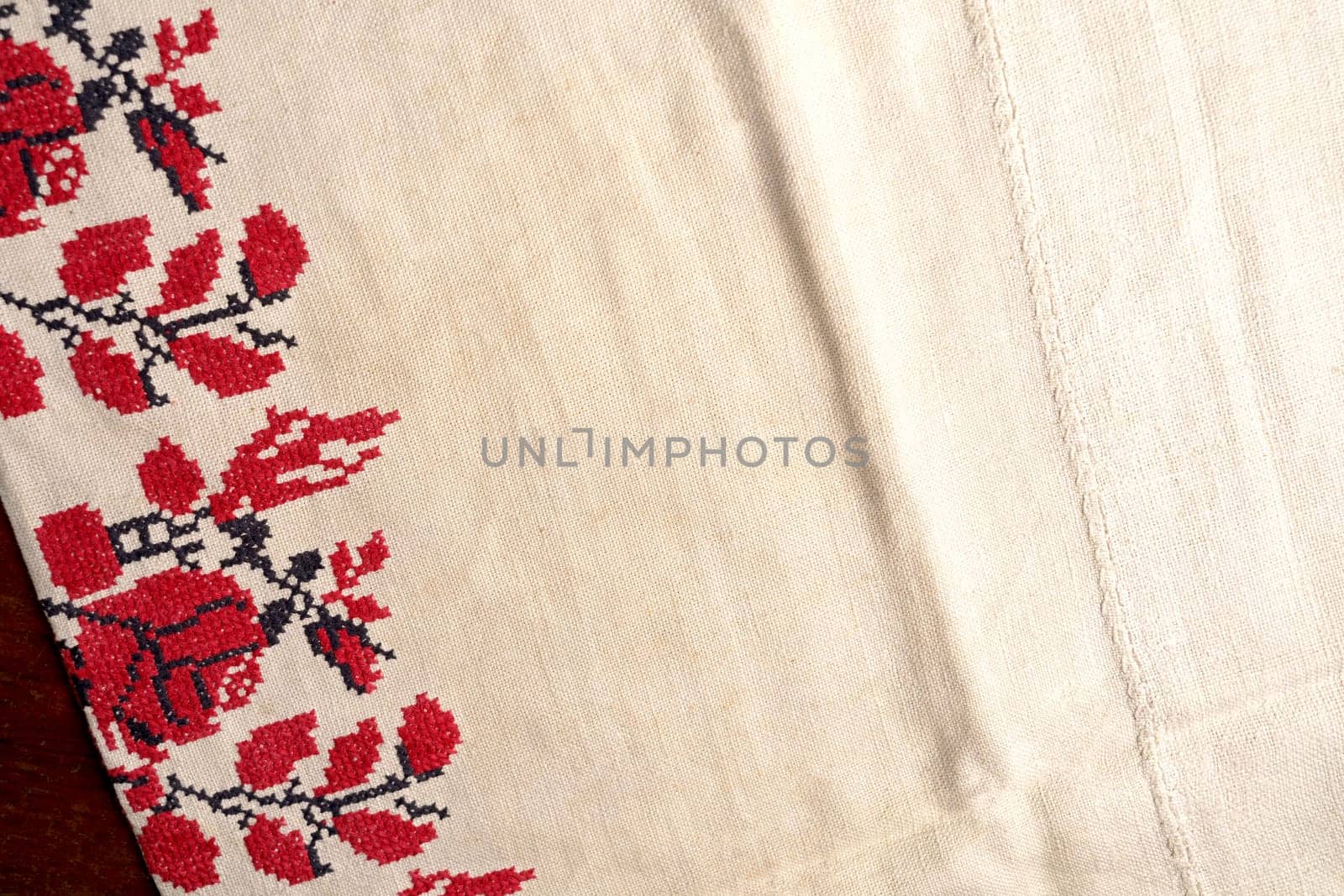 Embroidered good like old handmade cross-stitch ethnic Ukraine pattern. Ukrainian rushnyk . Red version over white background.. Black and red embroidery. Beige white farmhouse style stripes texture. Kitchen table with red towel. Top view with copy space by aprilphoto