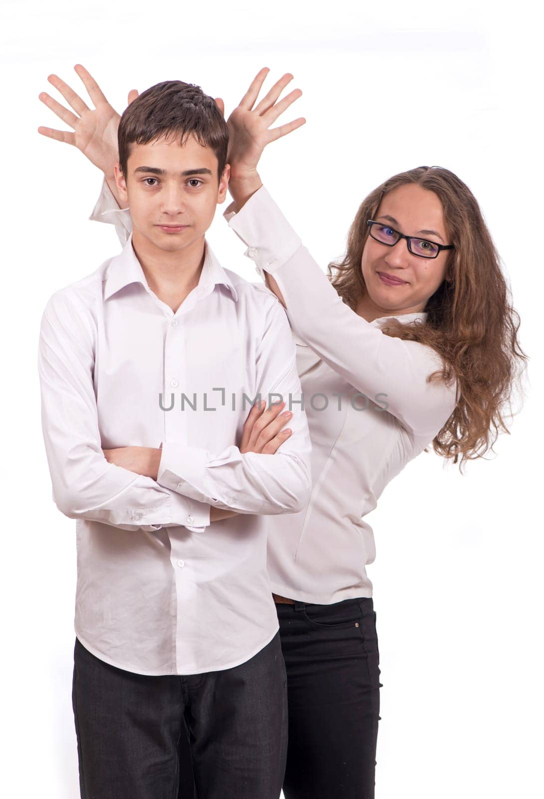 schoolchildren are joking building horns. Portrait of cute schoolchildren. A girl and a guy in school clothes are having fun and joking, playing tricks on each other. The girl shows the horns. Studio isolated on white background. by aprilphoto