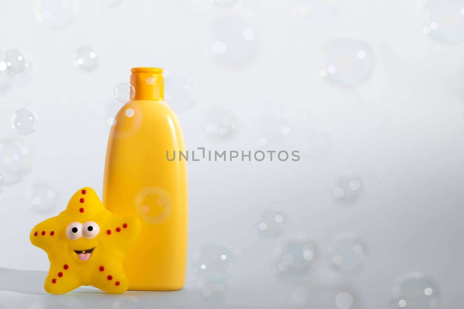 Baby bath foam or liquid soap with yellow star fish and many flying soap bubbles on white background. Children's bath time concept. Copy space