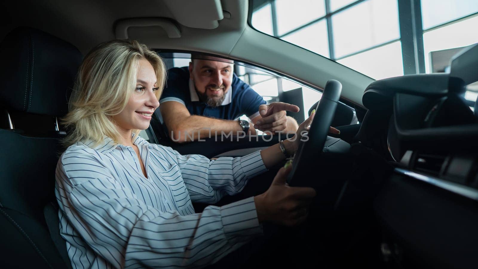 Happy caucasian couple chooses a new car in a car dealership for his wife. A young woman is driving