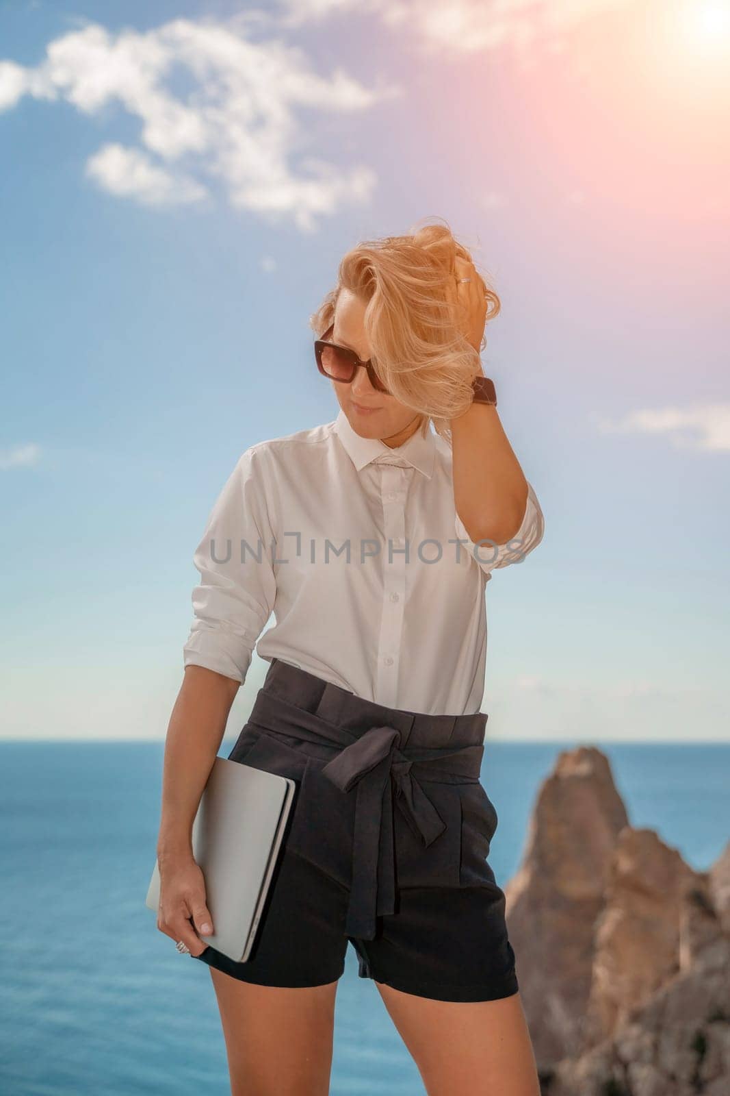 Freelance women sea working on a computer. Pretty middle aged woman with computer and phone outdoors with beautiful sea view. The concept of remote work. by Matiunina