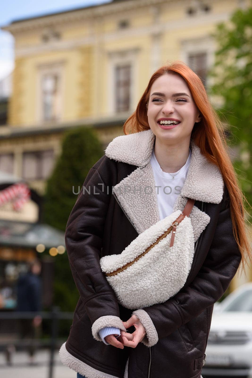 a red-haired girl in a leather jacket. cheerful woman with long red hair poses for a photographer.